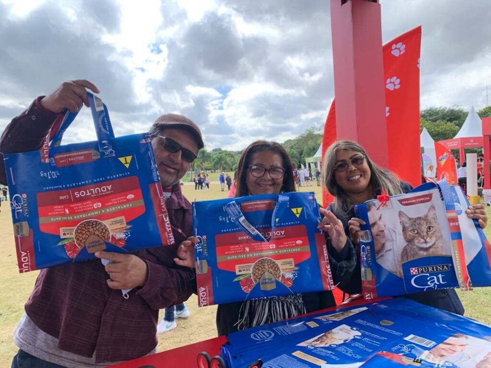 Três participantes sorrindo com suas ecobags feitas de saco de ração