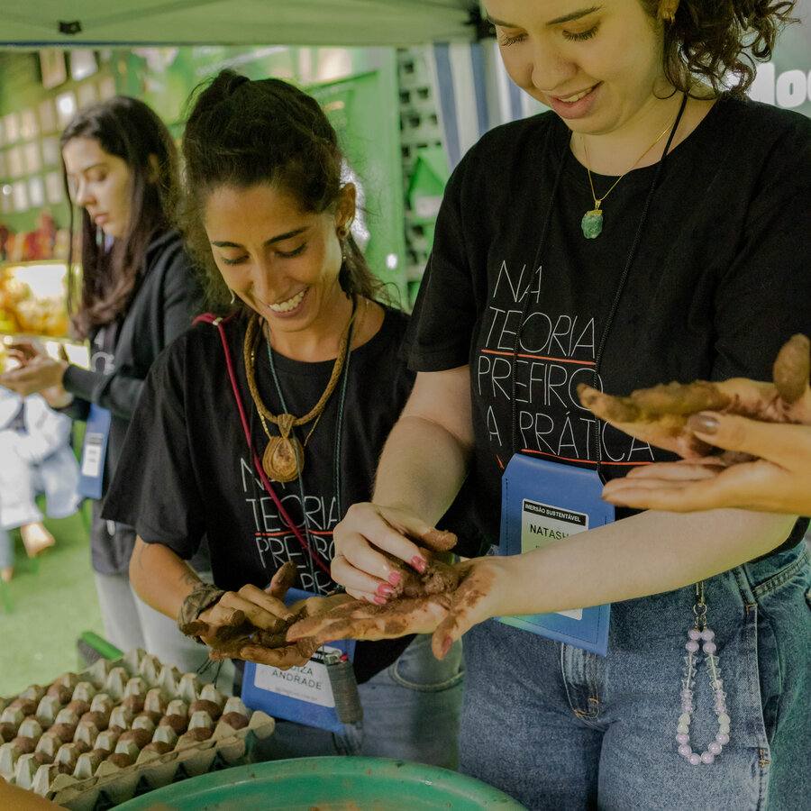 Grupo de participantes moldando bombas de sementes com as mãos, com bandejas de ovo ao fundo