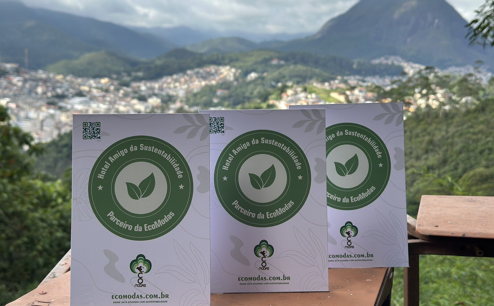 Três certificados do Selo Verde Hotelaria — Hotel Amigo da Sustentabilidade, Parceiro da EcoModas — expostos com vista para Nova Friburgo