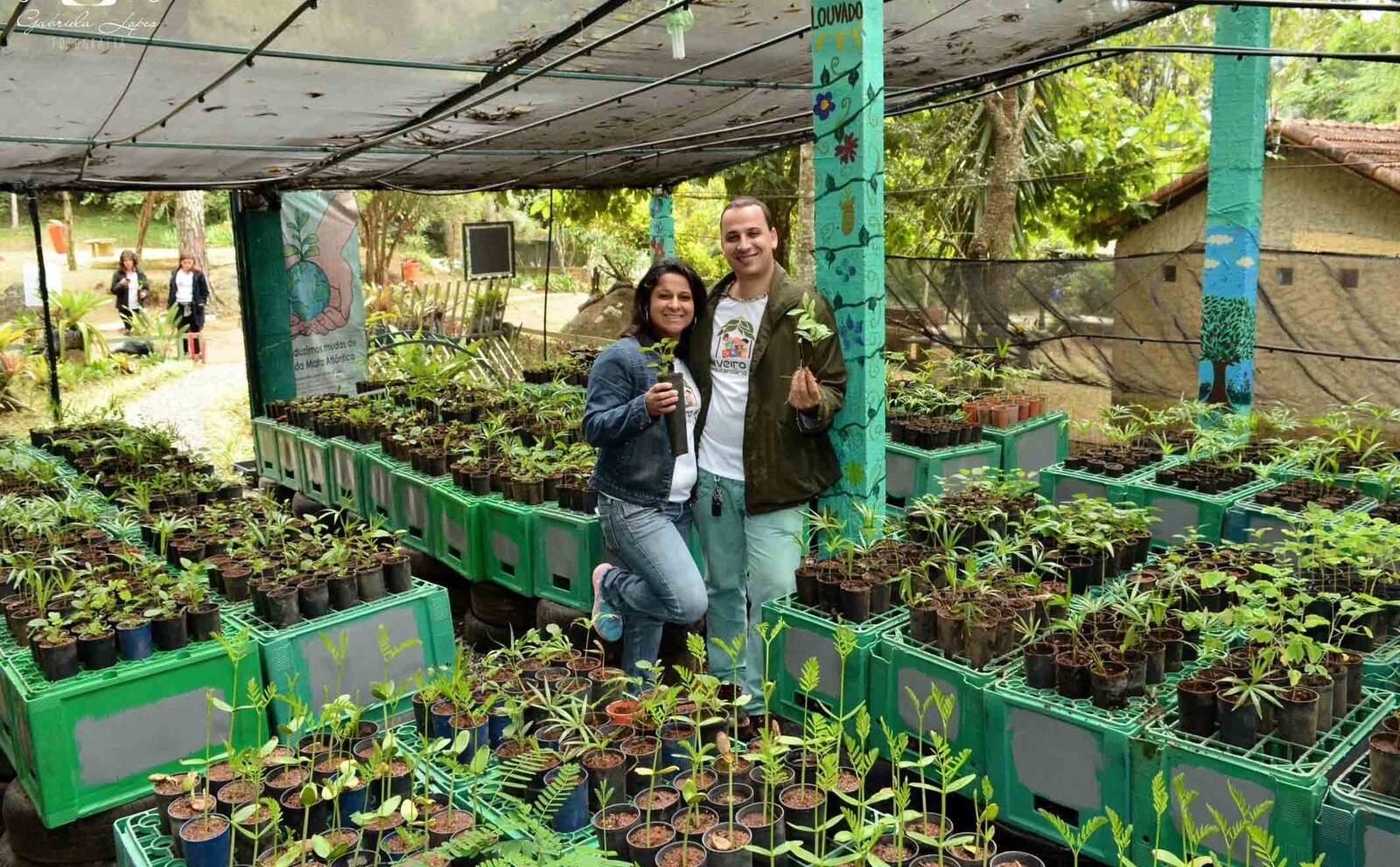 Alex e Adriana, fundadores da EcoModas, dentro do Viveiro Educandário, cercados por centenas de mudas de árvores nativas em cones de linha