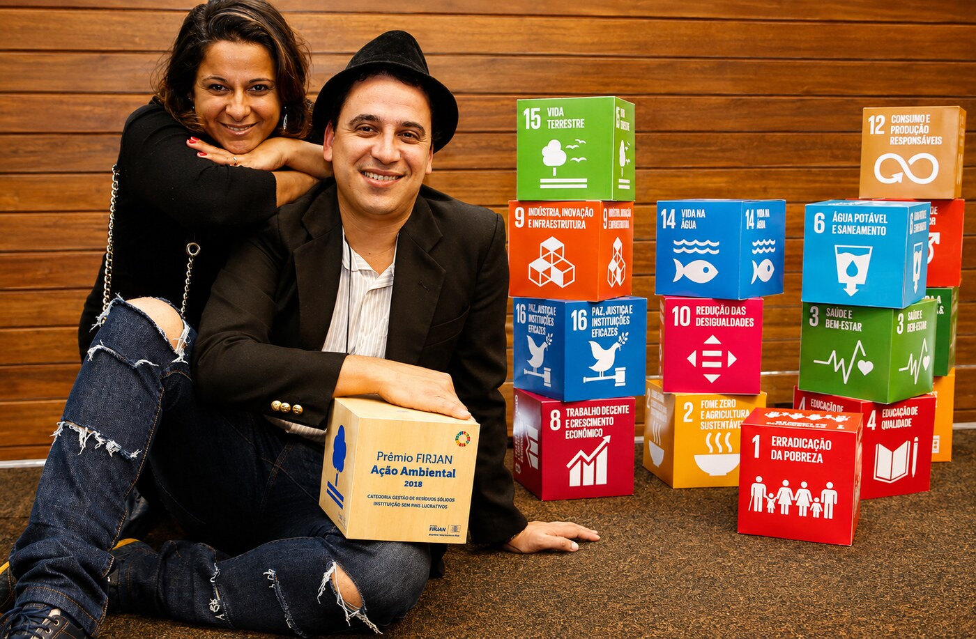 Alex e Adriana, fundadores da EcoModas, sorrindo ao lado do Prêmio Firjan de Ação Ambiental e dos selos das ODS